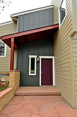 View of home entrance with black metal siding around the door and tan James Hardie siding around the garage 