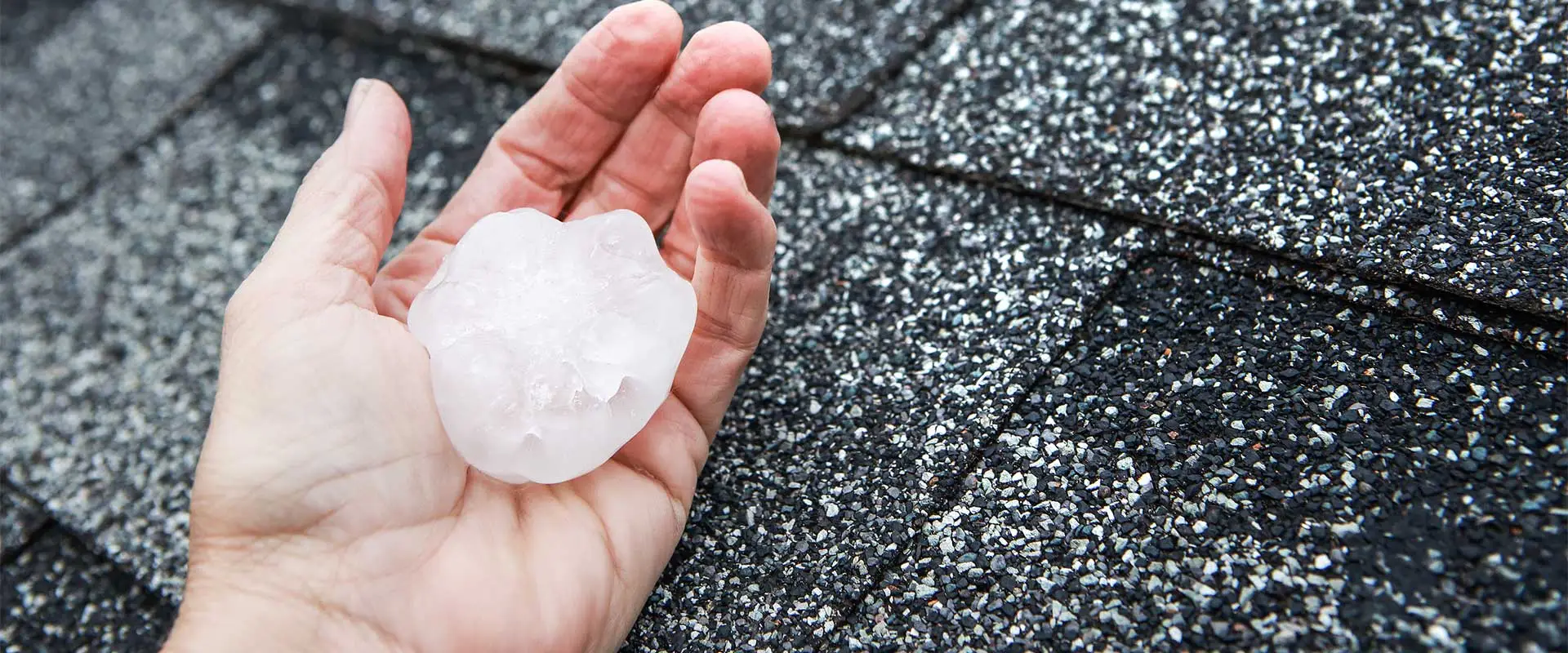 Closeup of a hand showing hail damage roof | Northern Lights Exteriors