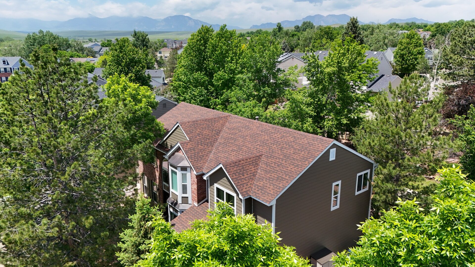 Aerial view of a Louisville, Colorado home with a completed asphalt shingle roof replacement, surrounded by mature trees with the Front Range in the distance.