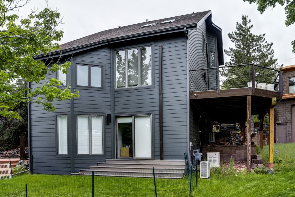 Large picture windows and a sliding glass door on a home in Morrison, Colorado, installed by Northern Lights Exteriors alongside dark fiber cement lap siding and an elevated deck
