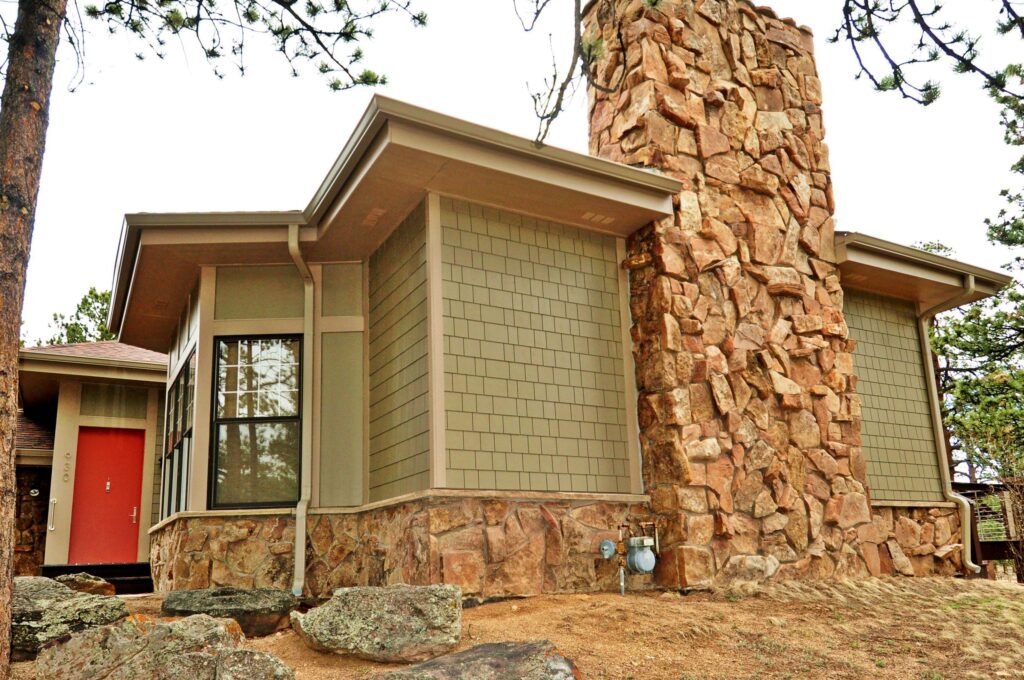 Fiber cement shingle siding with stone veneer wainscot and a full stone chimney on a mountain home in Estes Park, Colorado, installed by Northern Lights Exteriors among ponderosa pine