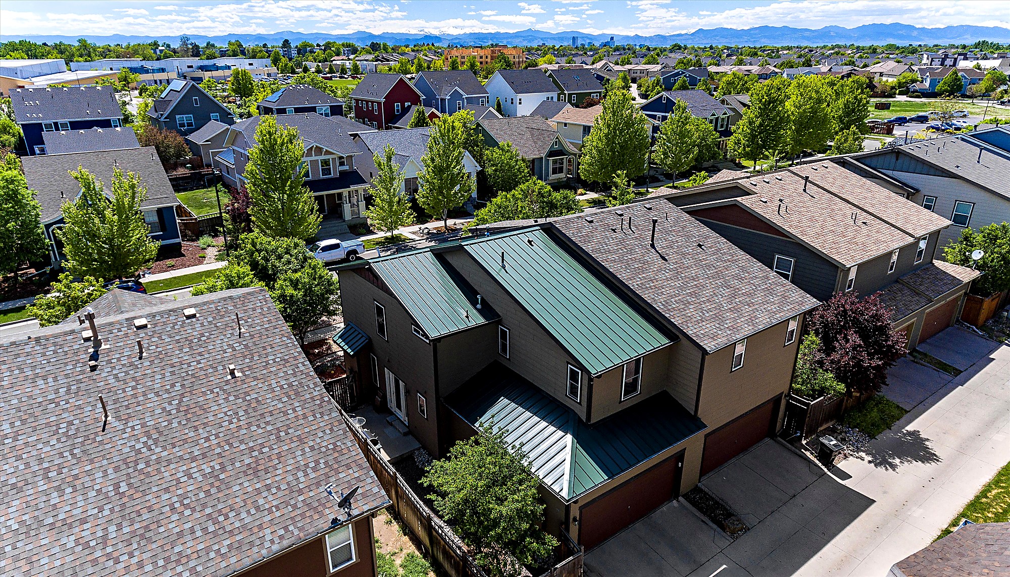 Aerial view of a standing seam metal roof installation on a Denver, Colorado home, combined with architectural asphalt shingles, with the Denver skyline and Front Range foothills behind