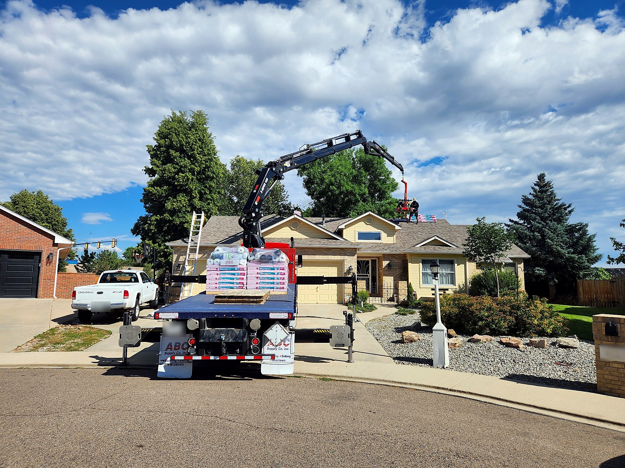 Crane truck lifting pallets of shingles onto the roof during a roof replacement in Longmont, Colorado, with the Northern Lights Exteriors crew working on the roof