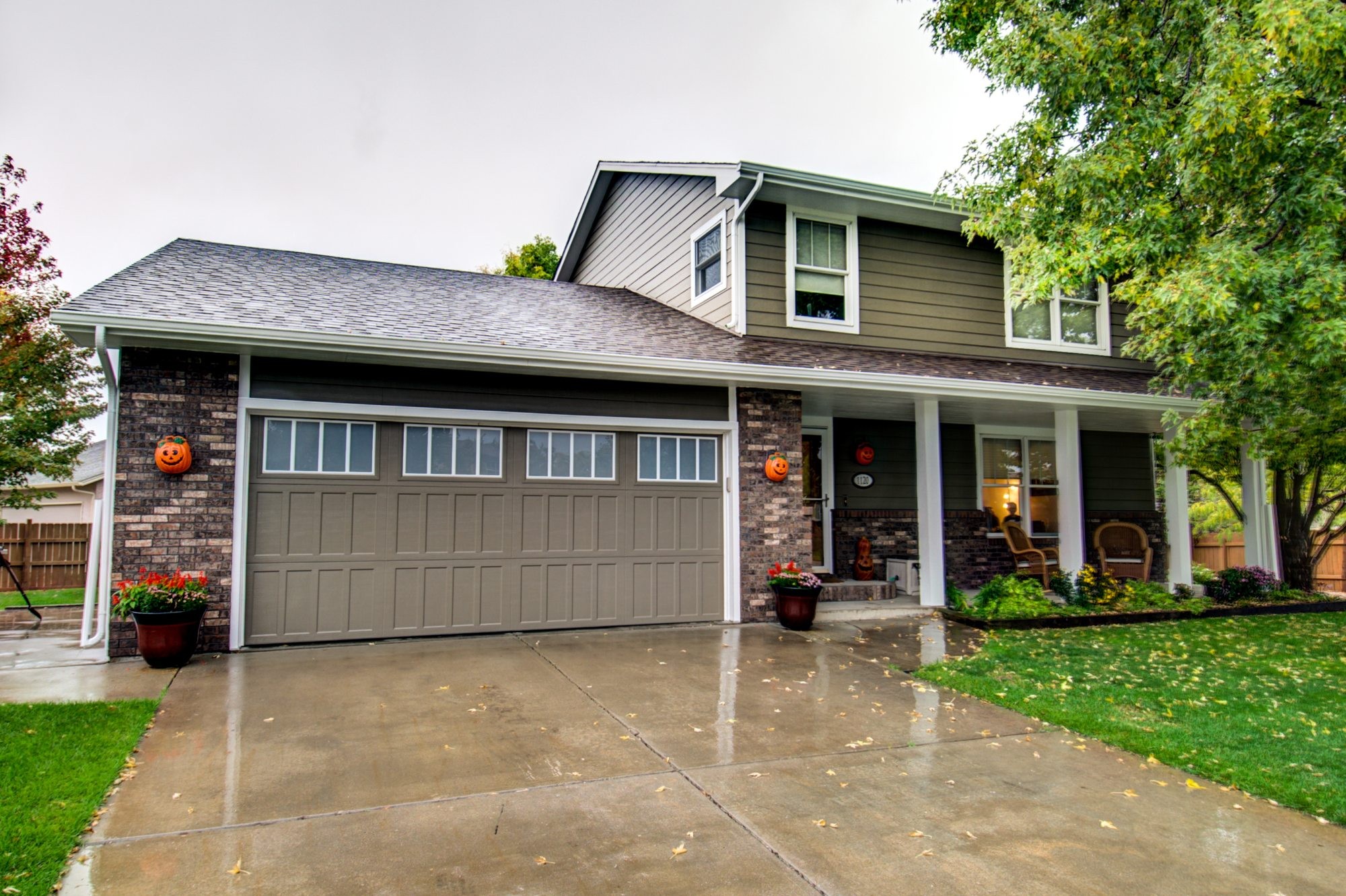 Two-story home in Windsor, Colorado with architectural asphalt shingle roofing, seamless gutters, sage-green lap siding with a board-and-batten gable, brick wainscot and a covered front porch.
