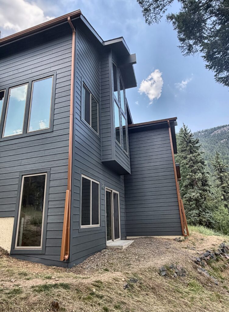 Black-framed windows and a two-story glazed corner on a home in Evergreen, Colorado, with James Hardie Iron Gray fiber cement siding and copper gutters installed by Northern Lights Exteriors