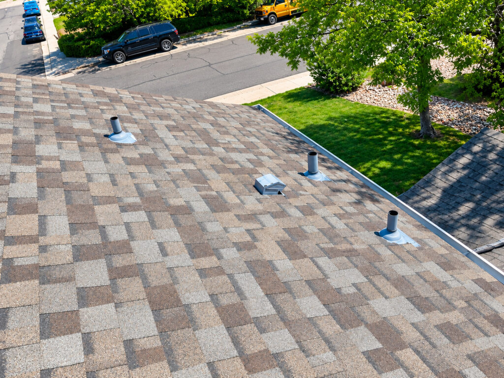 Close-up of new architectural asphalt shingle roof with pipe boot flashing, roof vent, and seamless gutter installed by Northern Lights Exteriors in Thornton, CO