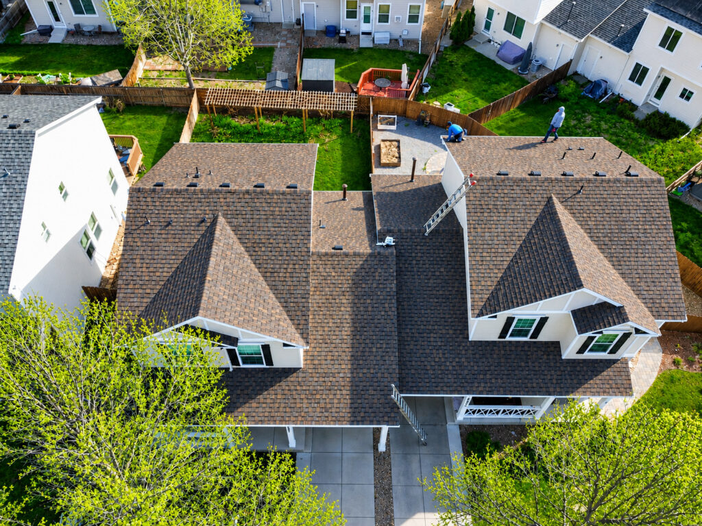 Aerial view of new brown architectural shingle roofs and white gutters installed by Northern Lights Exteriors on HOA homes in Thornton, CO after hail damage